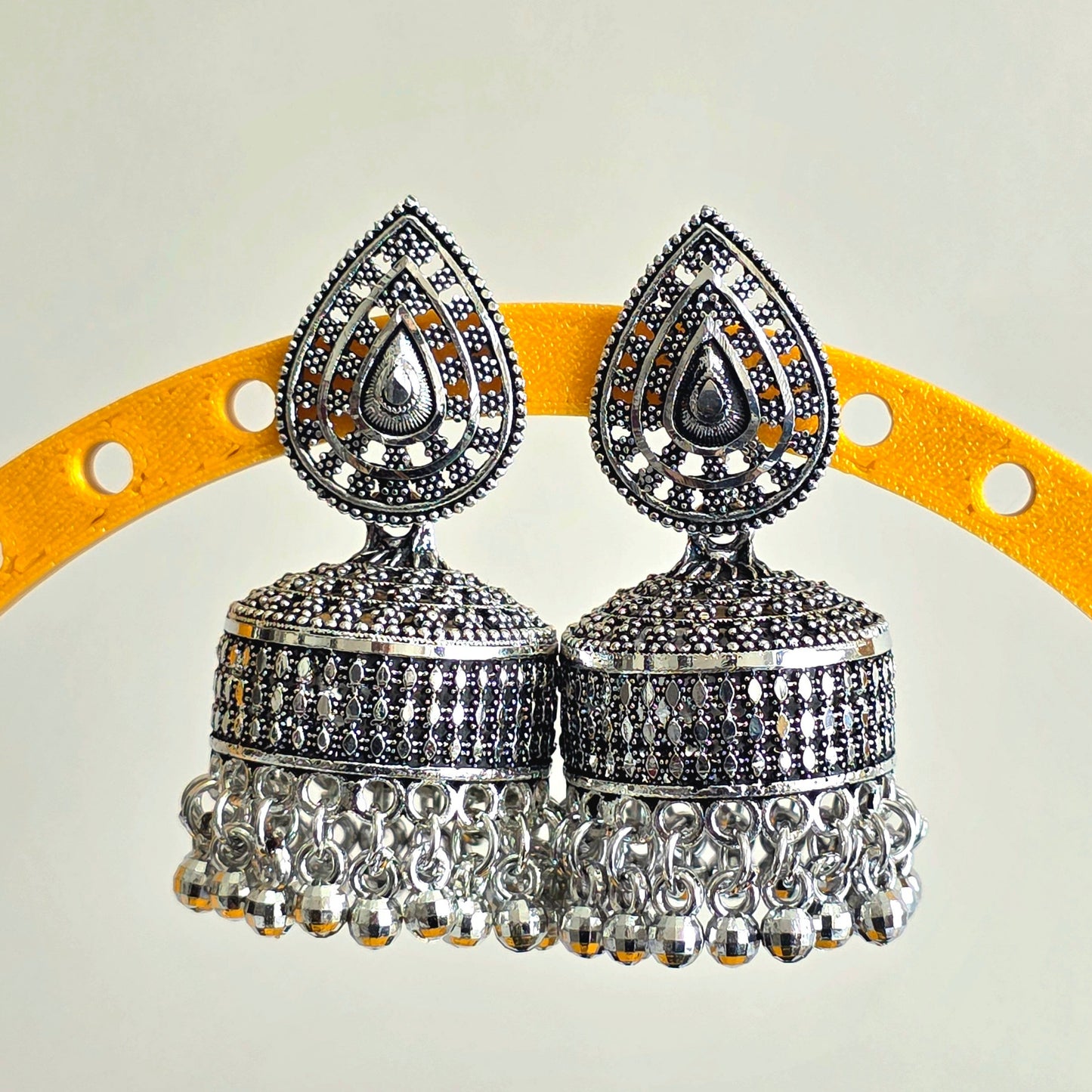 Silver jhumka earrings on a yellow and gray background