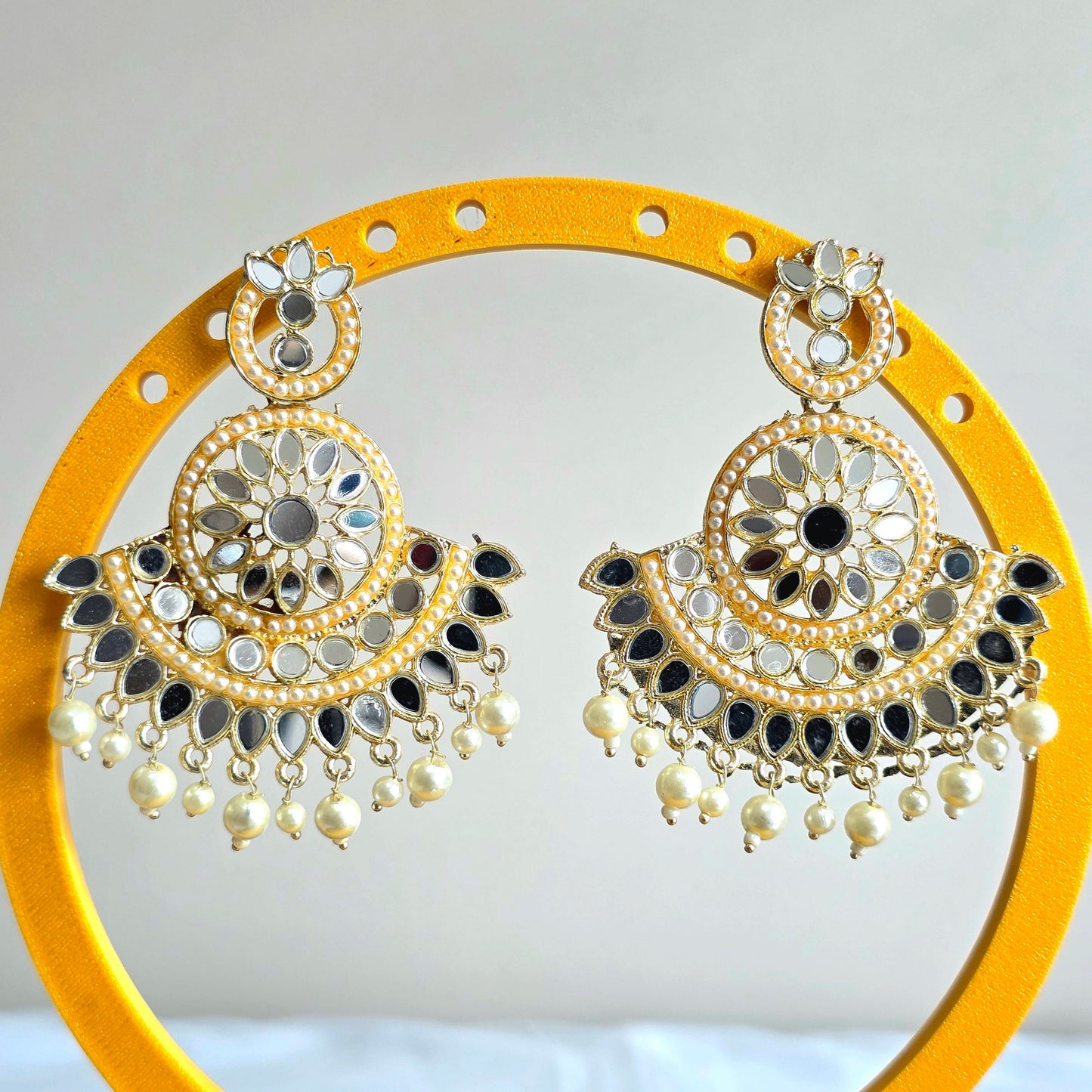Decorative earrings on a yellow stand with a white background