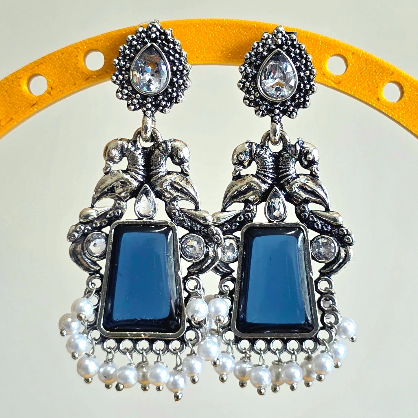 Pair of earrings with blue stones and pearl accents on a yellow stand.