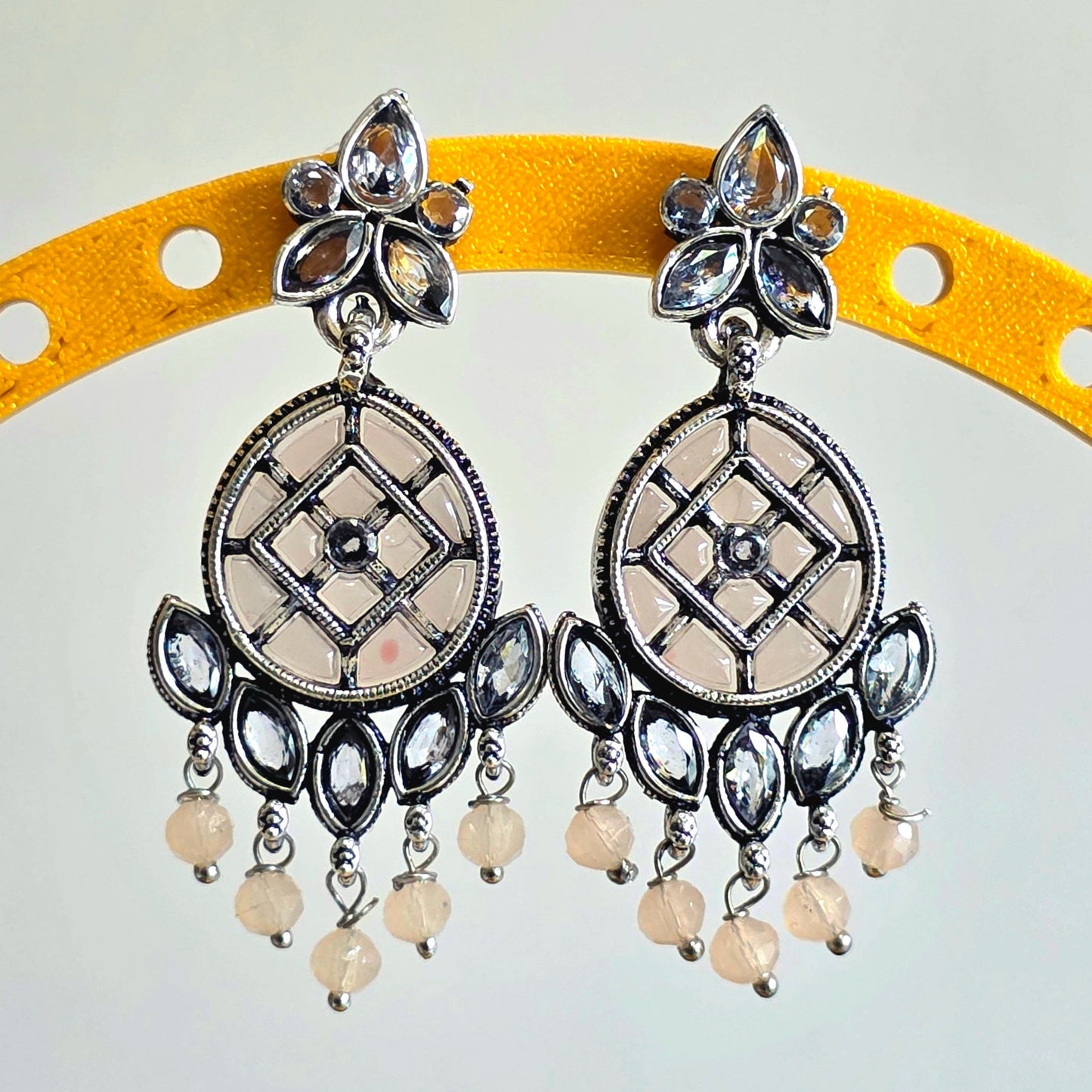 Pair of silver earrings with circular designs and pearl-like beads on a yellow arch.