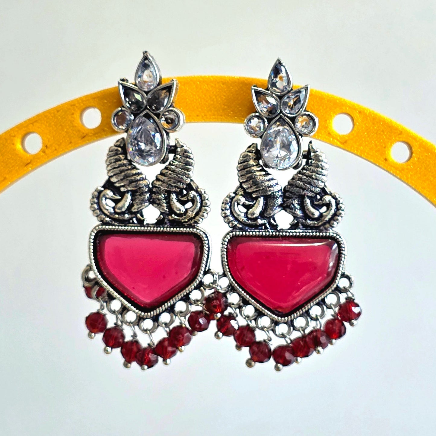 Pair of earrings with pink heart-shaped centers and silver detailing on a yellow circular background.