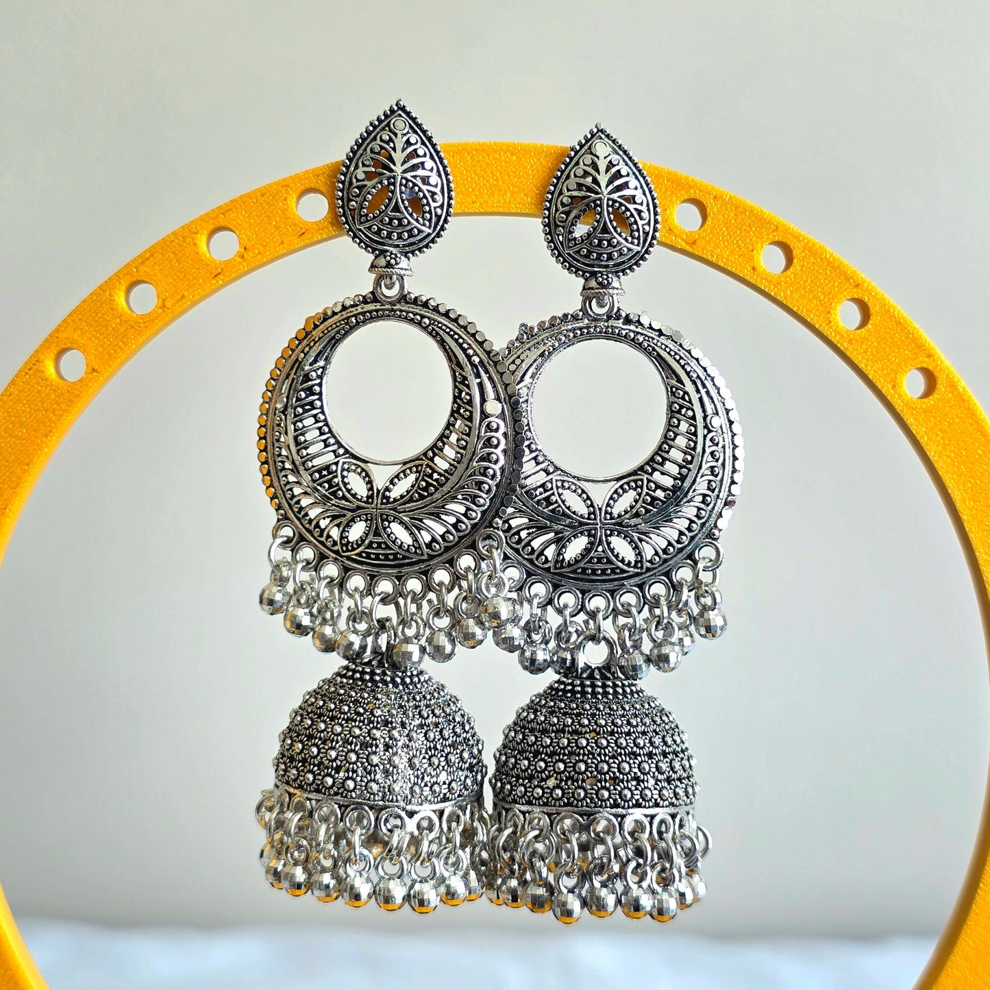 Silver earrings with intricate designs on a yellow circular stand against a light gray background