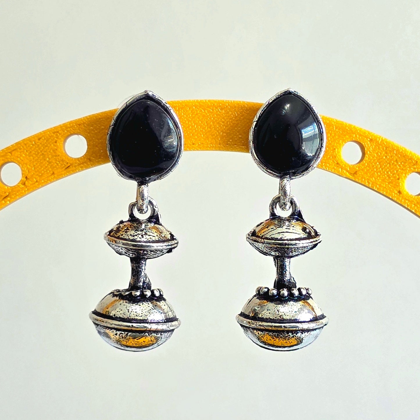 Pair of silver earrings with black stones on a yellow arch background
