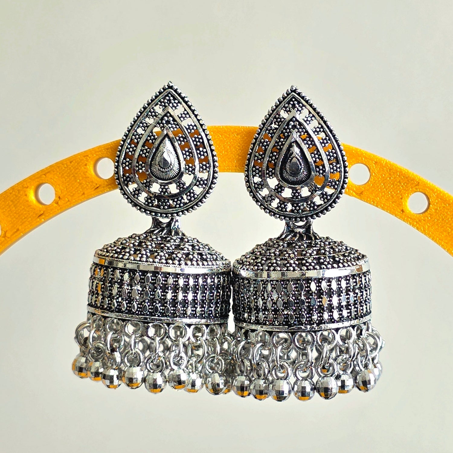 Silver jhumka earrings on a yellow and gray background