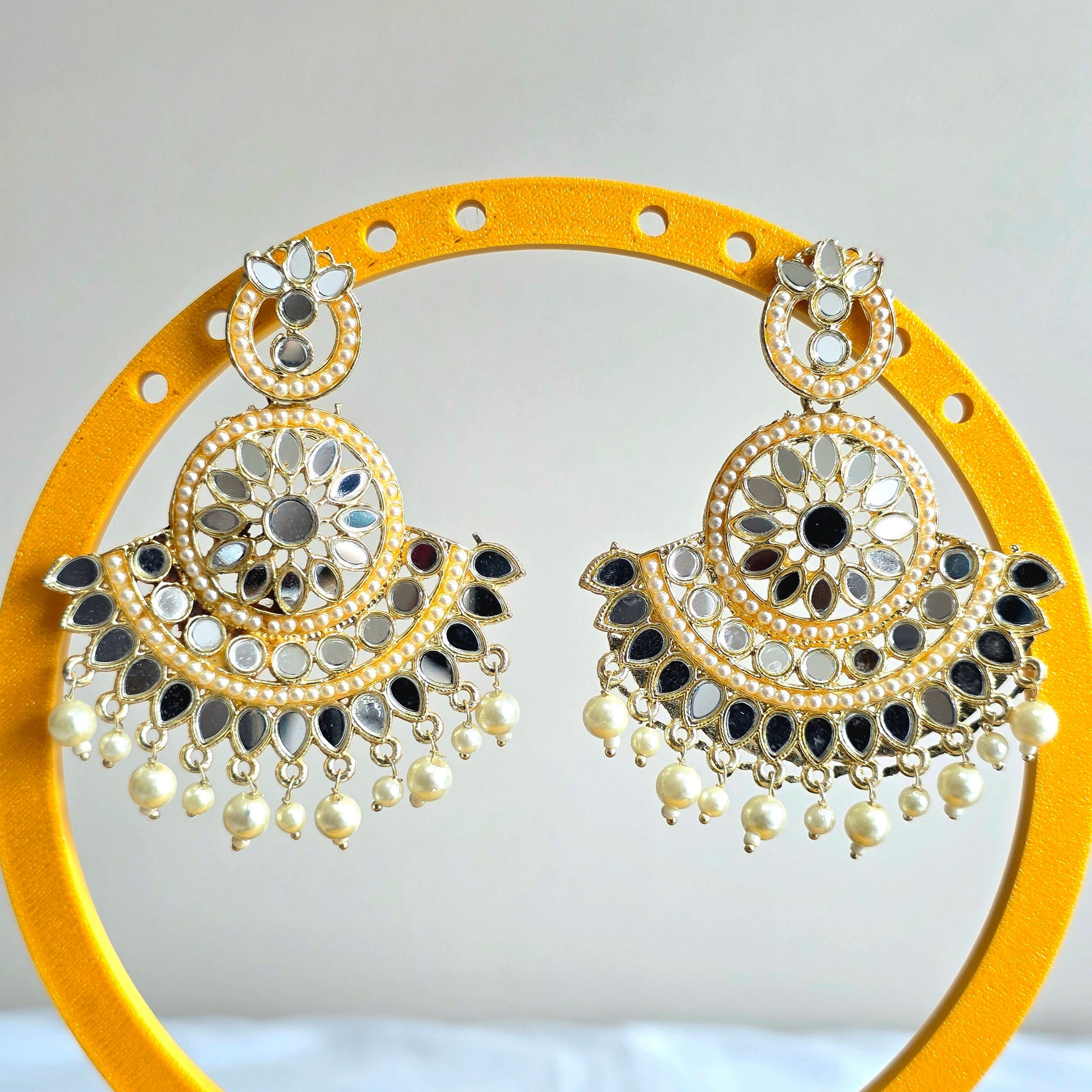 Decorative earrings on a yellow stand with a white background