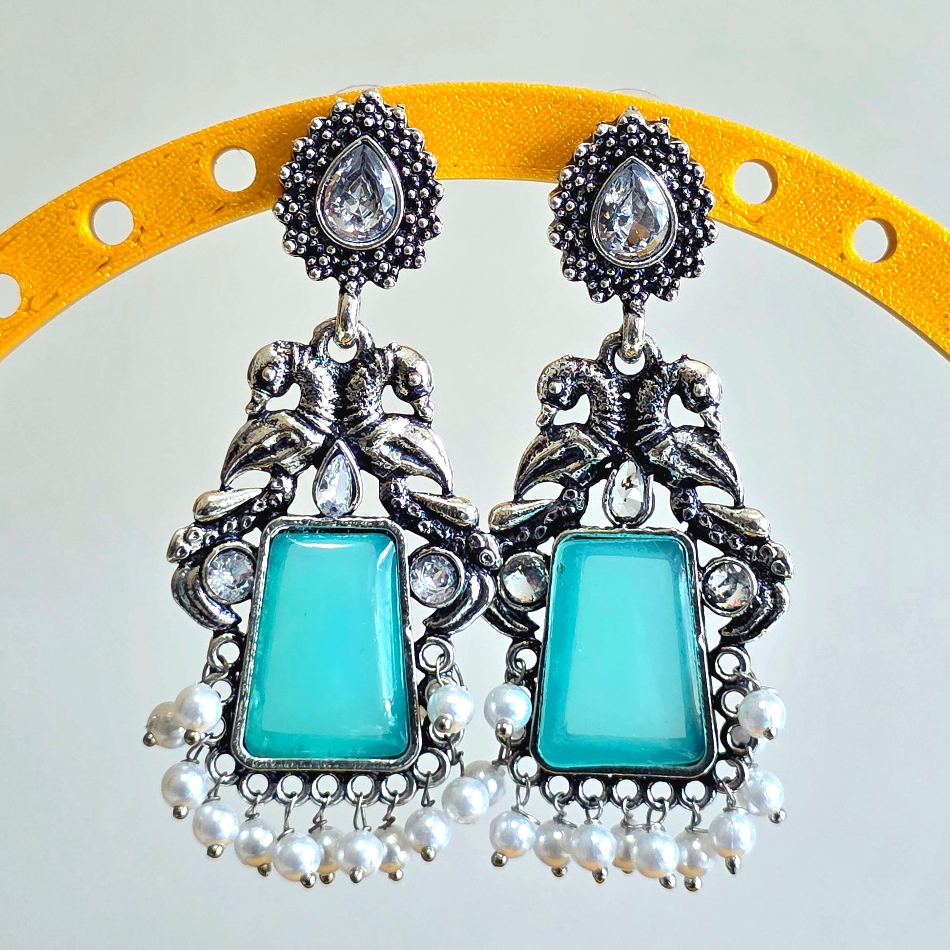 Pair of earrings with blue stones and silver accents on a yellow and white background