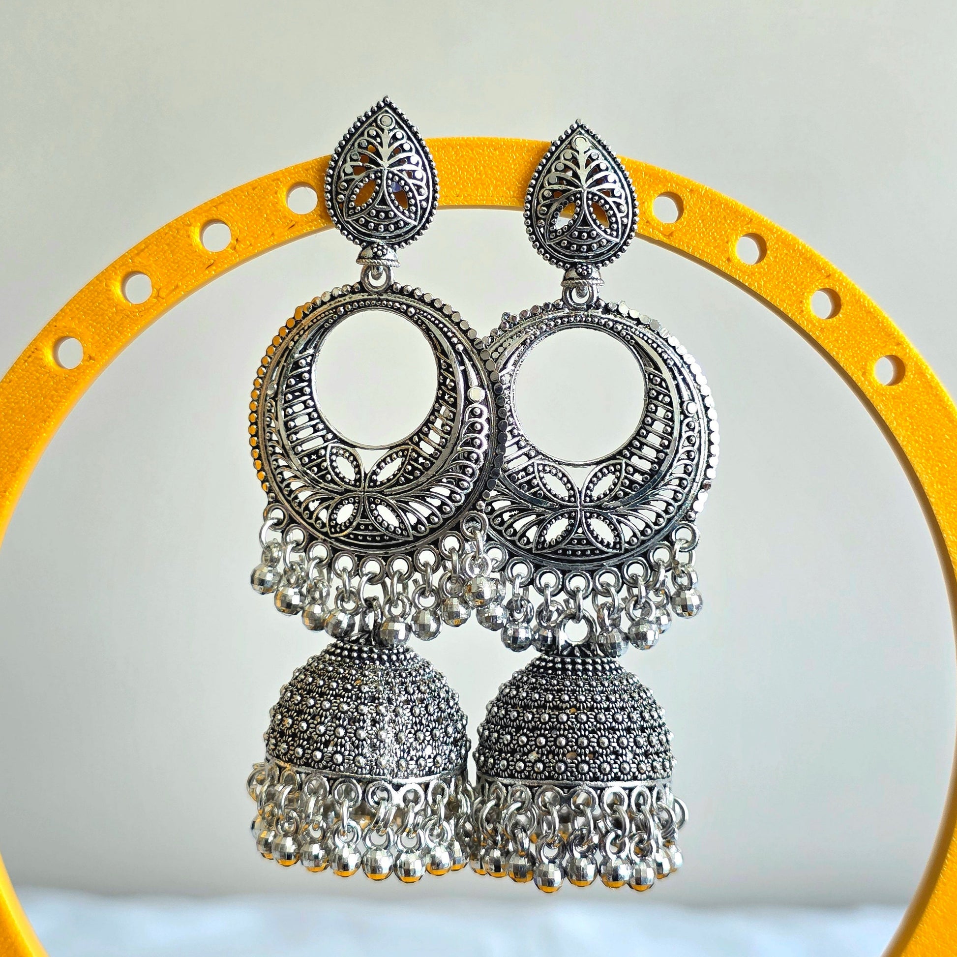 Silver earrings with intricate designs on a yellow circular stand against a light gray background