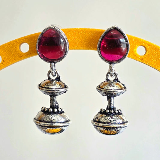 Pair of silver earrings with red gemstones on a yellow arch background